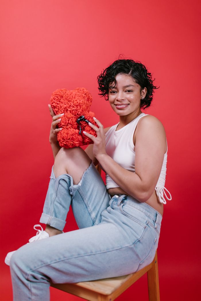 A joyful woman holding a decorative red teddy bear against a vibrant red backdrop.