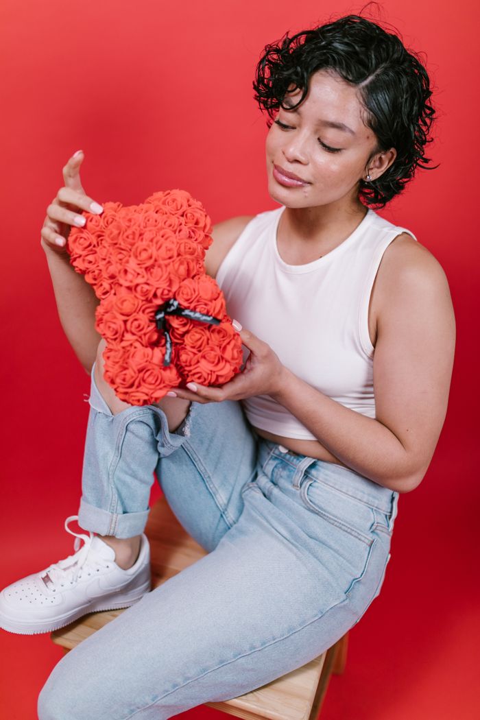 A woman in casual attire sits with a rose-covered bear, a perfect Valentine's gift.